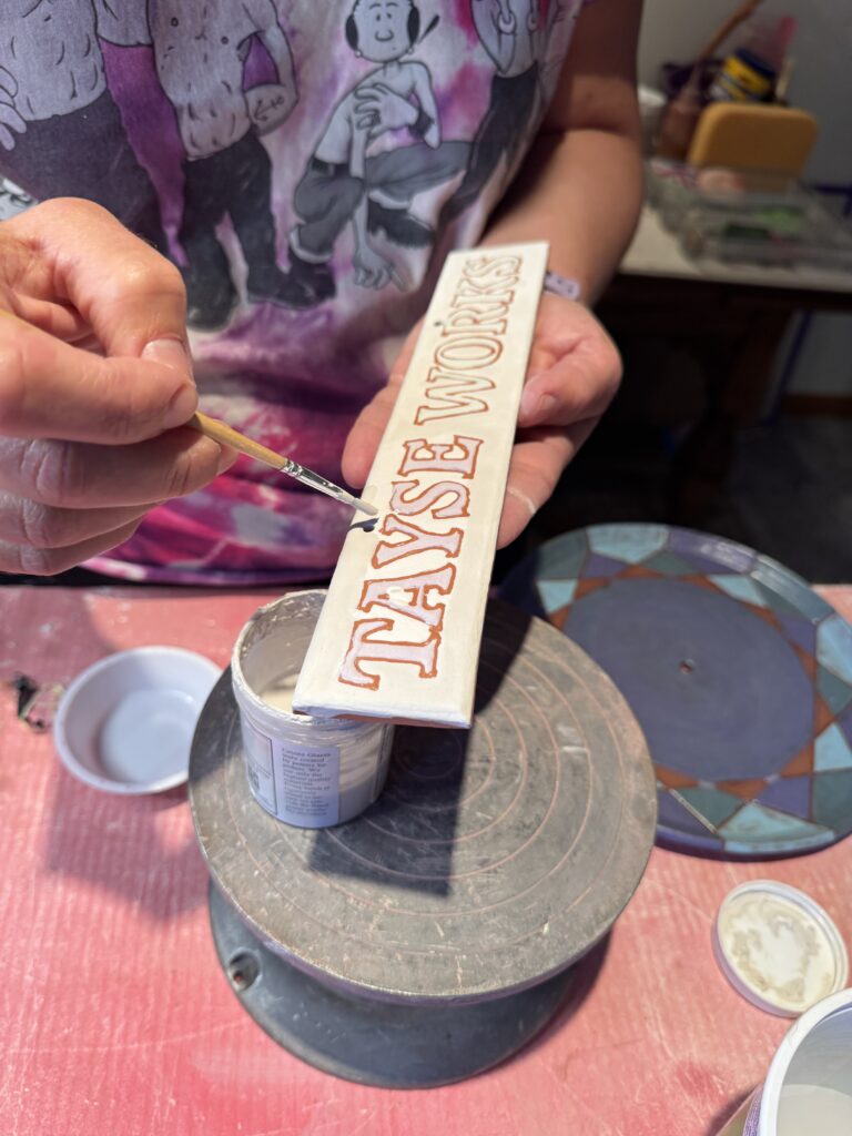 glazing a ceramic sign that says Tayse Works