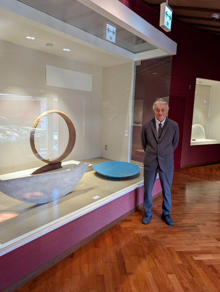 elder artist in suit stands next to exhibit of large geometric ceramics