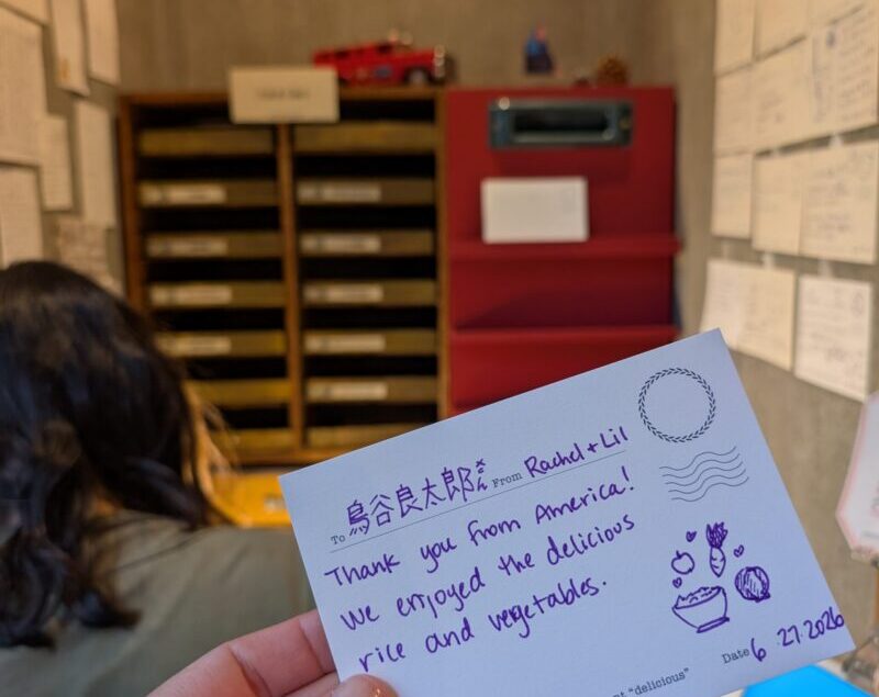 image of handwritten postcard in front of red japanese mail station